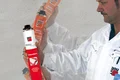Mann in Arbeitskleidung hält eine Dose Bau-Schaum vor grauer Wand, bereit zur Anwendung im Heimwerkerprojekt.