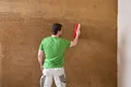 Mann glättet frischen Putz an der Wand mit einem roten Pinsel, Schritt für Schritt Anleitung auf Baumit für exzellente Ergebnisse.