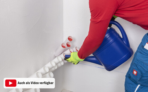 Person mit Schutzhandschuhen befüllt mit einer blauen Gießkanne Injektionstrichter in einer Wand zur Horizontalabdichtung.