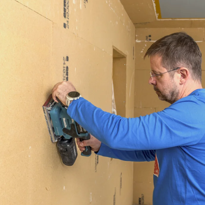 Heimwerker schleift Gipskartonwände mit einem Exzenterschleifer für glatte Oberflächen vor dem Anstrich in der Wohnungsrenovierung.