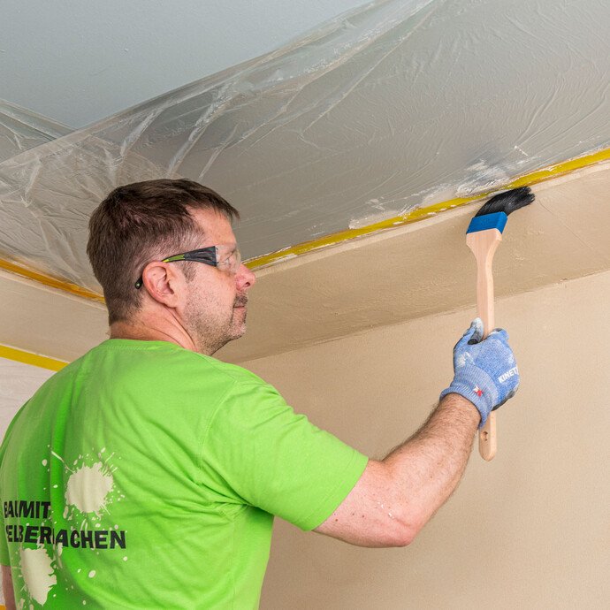 Heimwerker zieht Baumit Kalkin Kalkspachtel multifine an der Deckenoberkante mit einem Heizkörperpinsel eben ab – Kanten am Anschlusskeil der Innendämmung sauber begradigen, Baumit Selbermachen Anleitung.