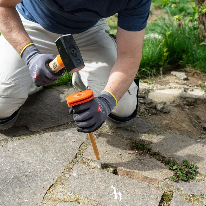 Person entfernt mit Hammer und Meißel losen Fugenmörtel zwischen Natursteinplatten.