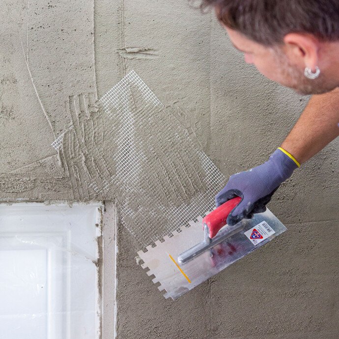 Beim Verputzen einer Wand wird im Eckbereich ein Streifen Armierungsgewebe in den frischen Putz eingesetzt und eingespachtelt.