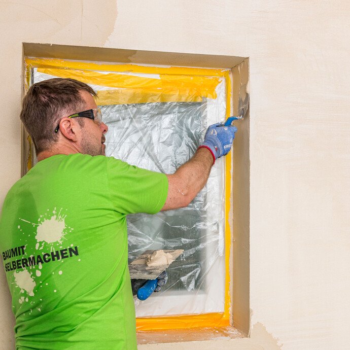 Heimwerker trägt Baumit Kalkin Kalkspachtel mit einer Glättkelle in der Fensterlaibung auf – Kalkspachtel auch in Laibungen sauber und gleichmäßig verarbeiten, Baumit Selbermachen Anleitung.