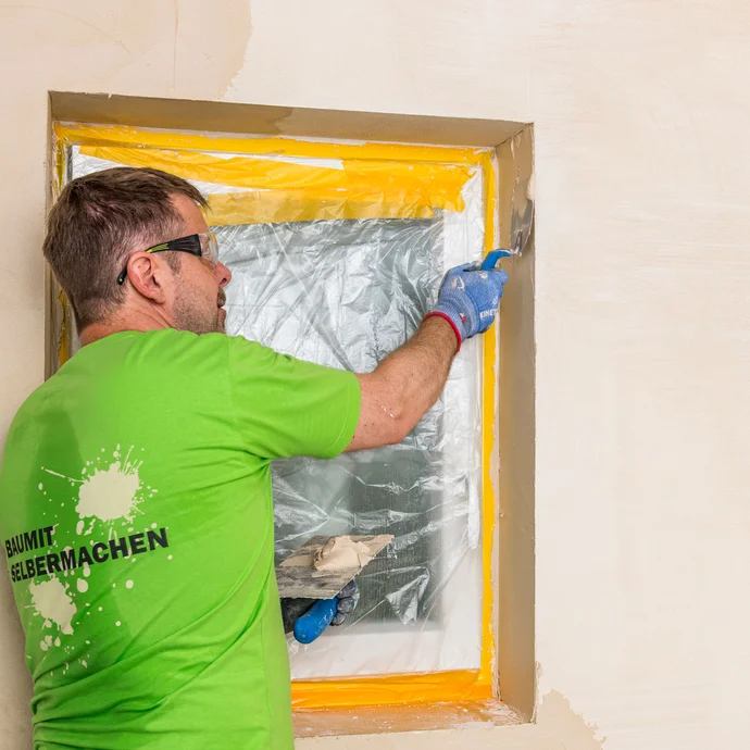 Heimwerker trägt Baumit Kalkin Kalkspachtel mit einer Glättkelle in der Fensterlaibung auf – Kalkspachtel auch in Laibungen sauber und gleichmäßig verarbeiten, Baumit Selbermachen Anleitung.
