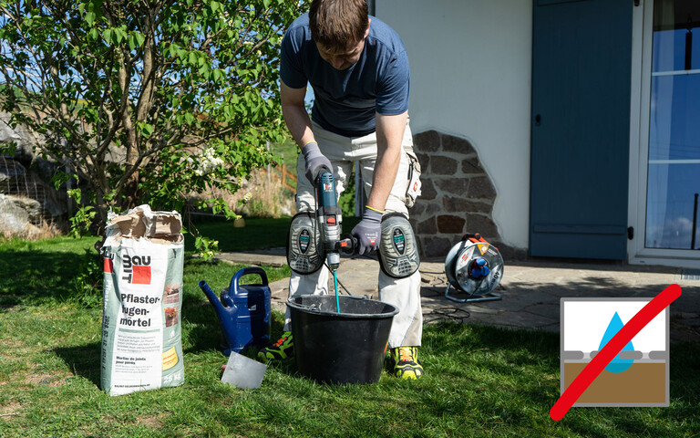 Person rührt mit einem elektrischen Rührgerät den Pflasterfugenmörtel im Garten an.