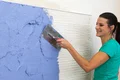 Frau trägt blauen Putz mit Kelle auf Wand auf, DIY-Projekt mit Baumit-Produkten, Schritt für Schritt Anleitung zur Wandgestaltung.