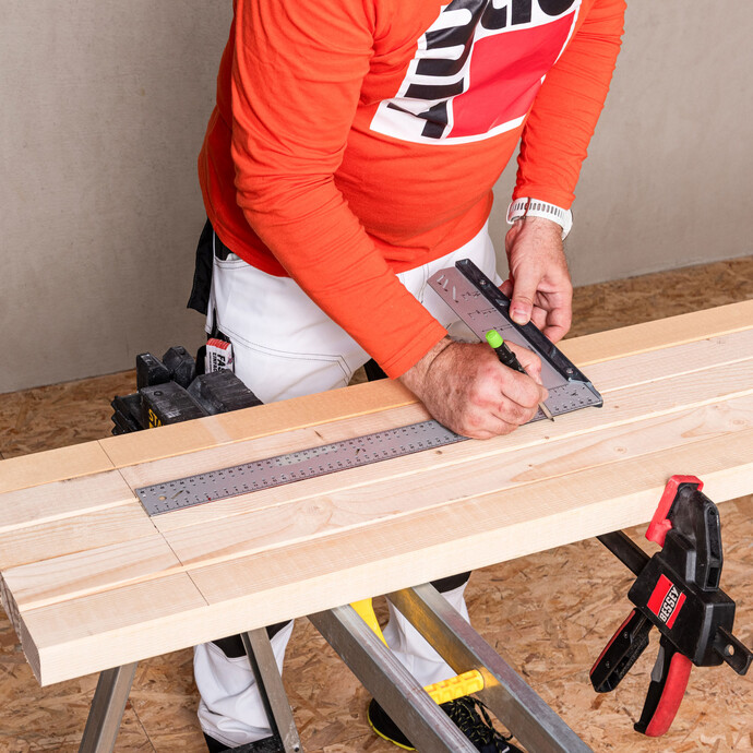 Heimwerker zeichnet die genauen Maße mit einem Stift und Winkel auf dem Kantholz ein, um das Holz in später auf die Länge zuschneiden zu können.