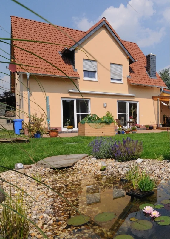 Ein modern renoviertes Einfamilienhaus mit frischer Fassadenfarbe neben einem gepflegten Garten mit kleinem Teich.