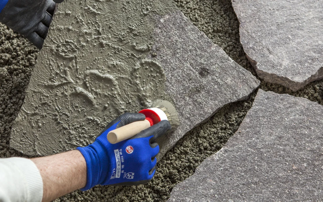 Verlegen von Natursteinen im Au&szlig;enbereich mit M&ouml;rtel; Handwerker gl&auml;ttet Oberfl&auml;che mit Pinsel.