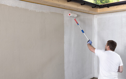 Mann trägt weiße Grundierung großflächig mit einer großen Farbrolle auf der Wand auf.