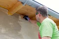 Mann trägt mit einer Bürste den Tiefengrund bzw. Putzfestiger unterhalb der Sparren auf.