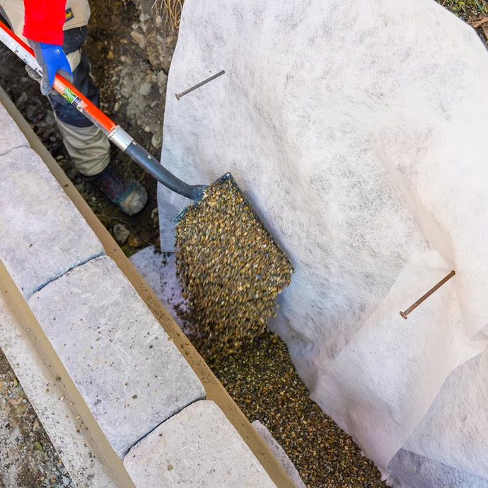 Schaufeln von Kies auf Geotextil zur Stabilisierung im Gartenbau und zur Vorbereitung von Pflasterarbeiten.