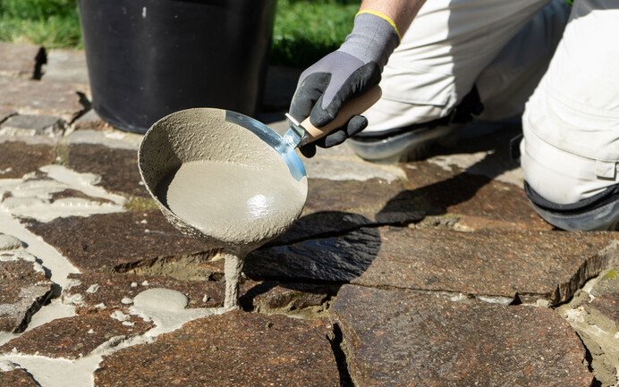 Pflasterfugenmörtel mit Gipserkelle o.ä. in den Fugen der Natursteine einbringen.