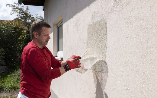 Heimwerker prüft die Tragfähigkeit des Untergrundes an der Fassade mit Hilfe des Abreißtests für die anschließende Sanierung. Dabei reißt er das Armierungsgewebe aus dem Fassadenspachtel von der Wand.