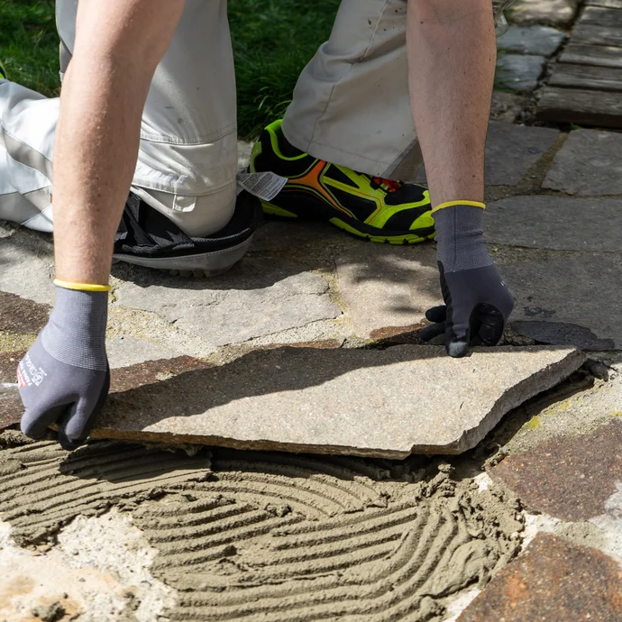 Eine Person setzt eine Natursteinplatte in den frischen Steinkleber.