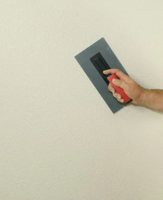 Hand glättet Wand mit Kelle für perfekten Putzauftrag, DIY-Projekt für Heimwerker mit Baumit-Produkten.