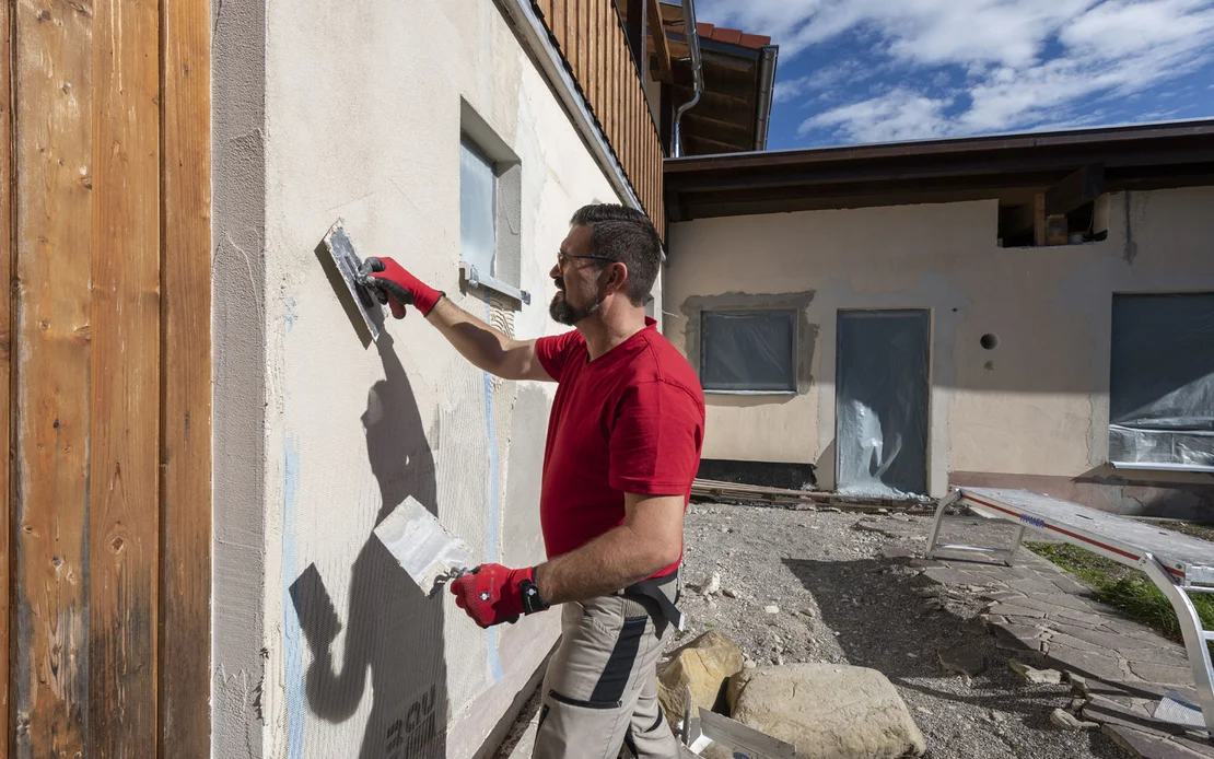 Heimwerker bettet das Gewebe fl&auml;chig mit der glatten Seite der Zahnkelle in den Armierungsm&ouml;rtel an der Fassade ein.