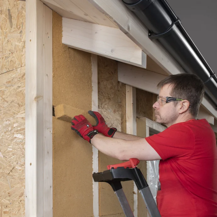 Heimwerker installiert Dämmmaterial an einer Wand, mit Holzrahmen und OSB-Platten als Unterkonstruktion.