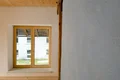 Fensterrahmen aus Holz in modernem Innenraum; frisch verputzte graue Wand rechts im Bild.