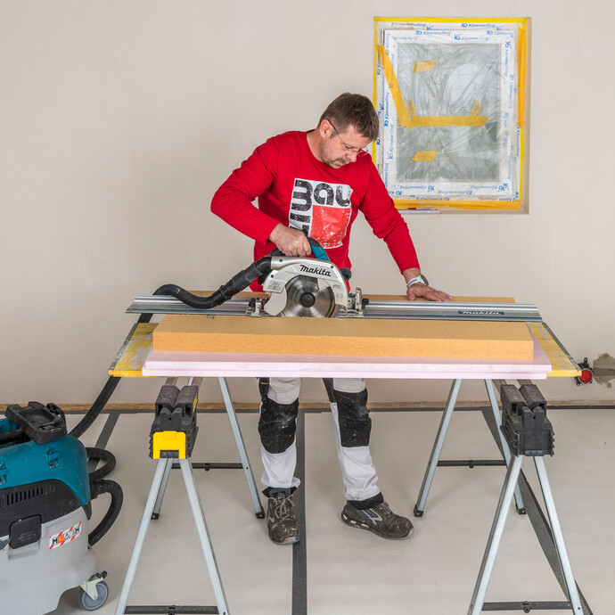 Heimwerker schneidet Baumit Holzfaserdämmplatte mit einer Handkreissäge und Führungsschiene gerade zu – sauberer und gerader Zuschnitt der Innendämmung mit angeschlossenem Industriestaubsauger, Baumit Selbermachen Anleitung.