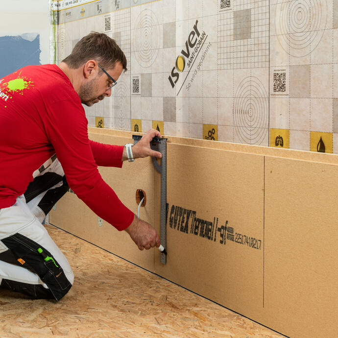 Heimwerker zeichnet Hilfslinien auf Holzfaserdämmplatte, um die Position der Traghölzer für die Verdübelung zu markieren. Innendämmung mit Holztragkonstruktion.