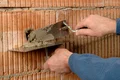Heimwerker trägt Mörtel auf Ziegelwand auf; Schritt für Schritt Anleitung für sicheres Verfugen und Verarbeiten von Baumaterialien.
