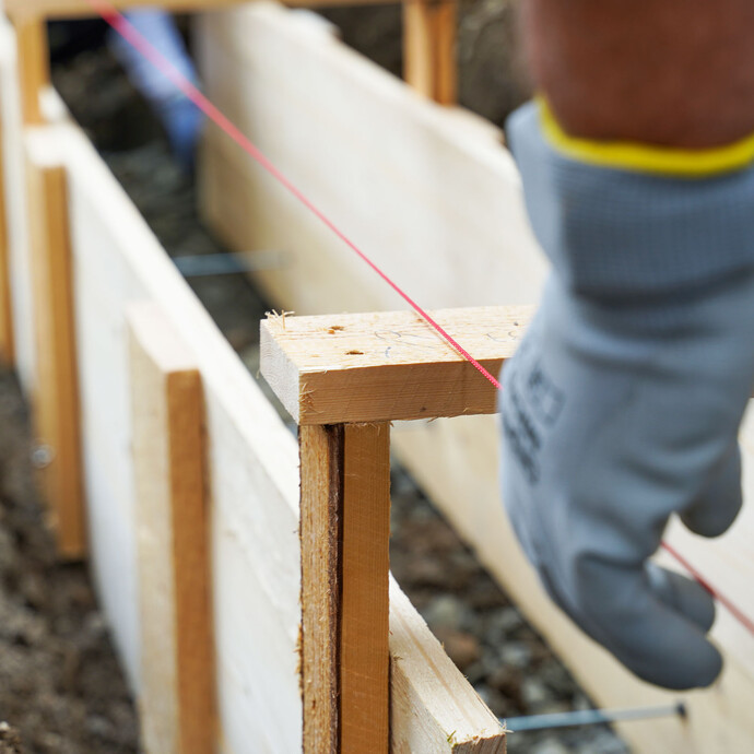 Zum Ausrichten des Schalungselements für das Fundament der Gartenmauer wird eine Richtschnur in der Baugrube gespannt.