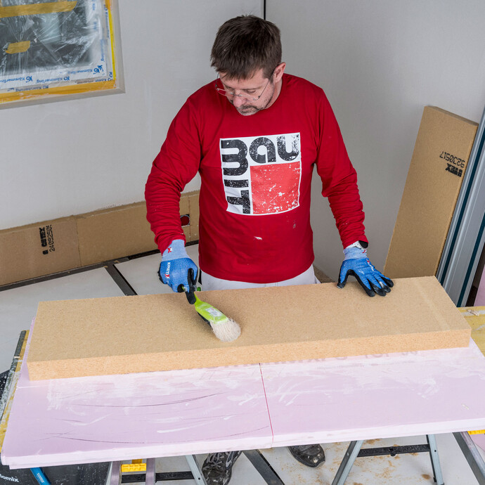 Heimwerker kehrt die Klebeseite einer Holzfaserdämmplatte mit einem Pinsel gründlich ab – Staub und Schmutz entfernen für eine optimale Haftung des Baumit Klebemörtels, Baumit Selbermachen Anleitung.