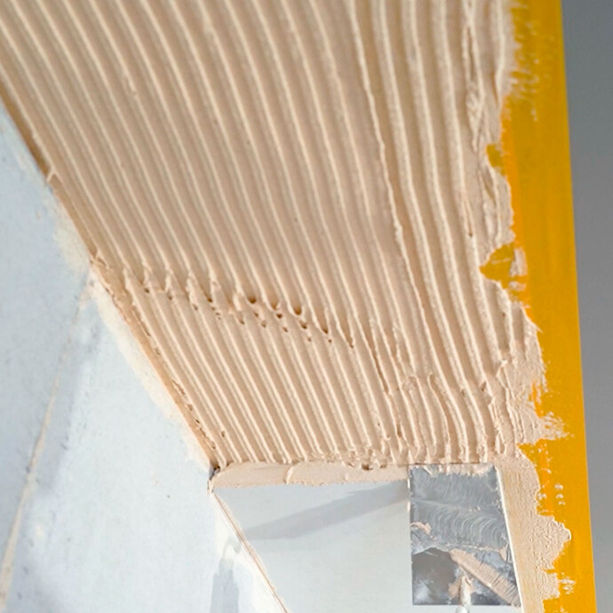 Mit einer Kelle wird Putz auf die Stoßkante des Anschlusskeils aufgetragen.