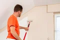 Heimwerker streicht Zimmerdecke mit Farbroller, Baumit, DIY-Tipps für Innenrenovierung.