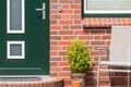 Eingangsbereich mit Backsteinwand, grüner Tür, Blumentopf und Stuhl, ideal für Heimwerker-Renovierungsprojekte.