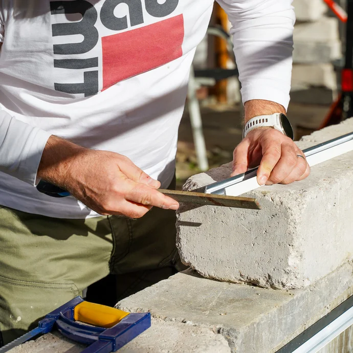 Handwerker feilt mit einer Eisenfeile die Schnittkanten des Abschlussprofils, um überstehende, scharfe Grate zu entfernen.