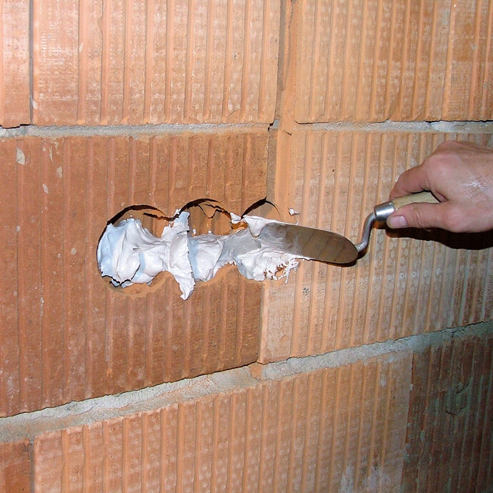 An der ausgefrästen Stelle im Ziegelmauerwerk, wird der spezielle Gips mit einer Kelle aufgetragen, um später die Elektrodose zu setzen.