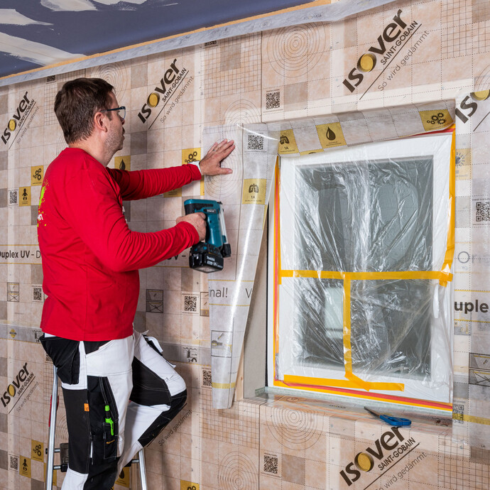 Das zugeschnittene Folienstück der Dampfbremse für die Laibung des Fenster befestigt der Handwerker von Baumit am gesetzten Kantholz des Fensters.