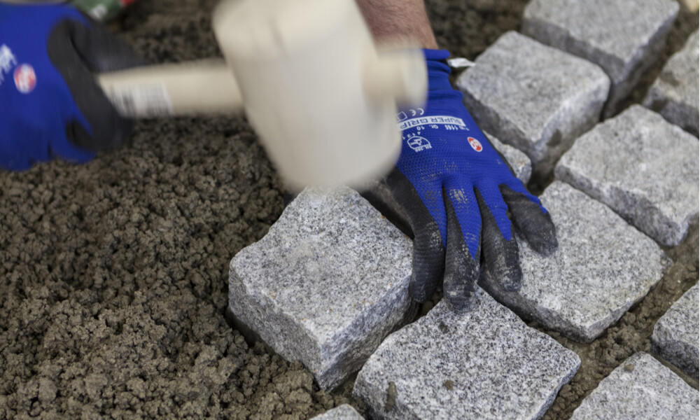 Granitpflasterstein mit Gummihammer in den frischen Pflasterdrainmörtel einklopfen