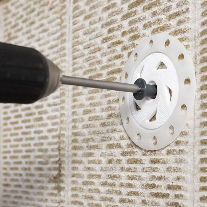 Bohrmaschine befestigt Dämmplatte mit Dübel an der Wand. Ideal für Heimwerkerprojekte rund um Dämmung und Renovierung.