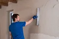 Heimwerker glättet Innenwand mit Richtlatte für gleichmäßige Oberfläche.