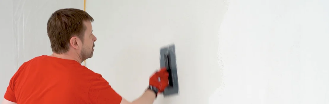 Mann verputzt eine Wand mit einer Glättkelle im Eigenbauprojekt.