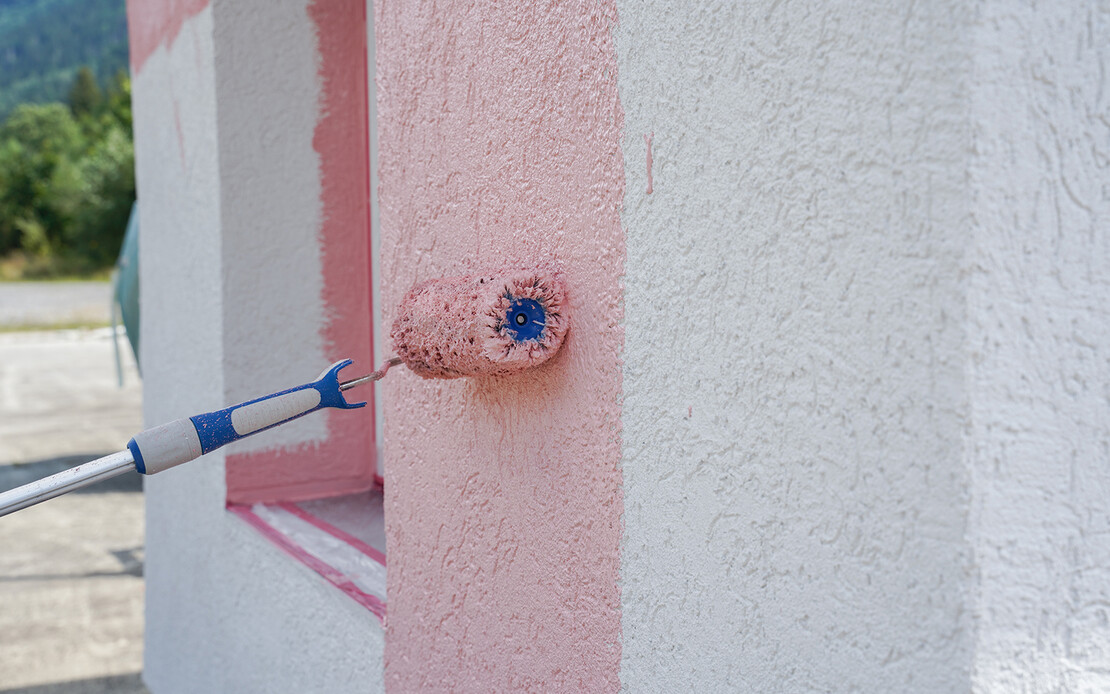 Eine weiße Wand wird mit einer großen Farbrolle rosa gestrichen.