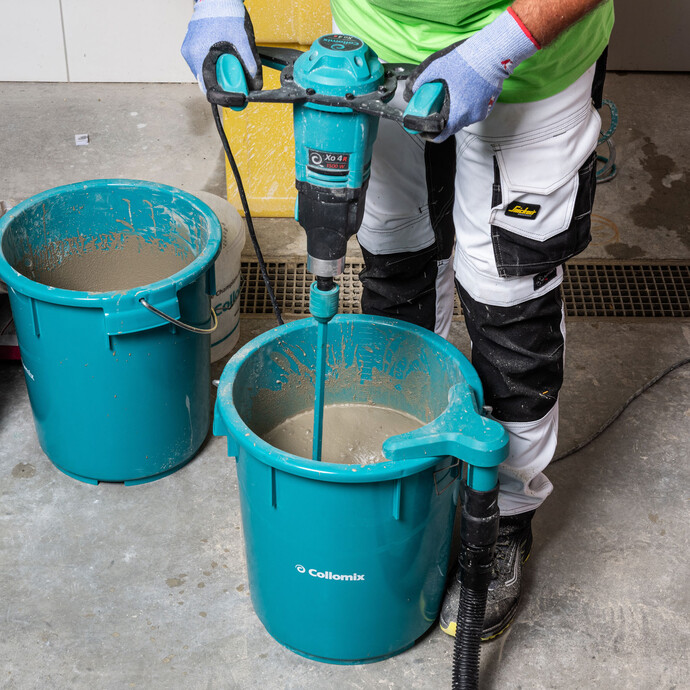 Person rührt die Ausgleichsmasse mit einem elektrischen Rührwerk von Collomix gründlich im Eimer durch.