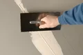 Hand, die Putz mit einer Kelle gleichmäßig auf eine Wand aufträgt.
