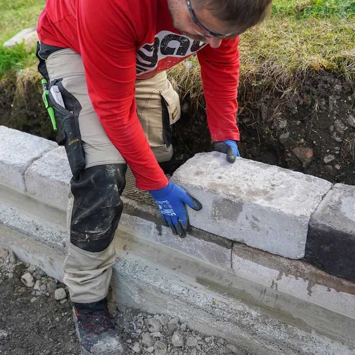 Mit beiden Händen wird ein gesetzter Betonstein auf der Mauer exakt ausgerichtet.