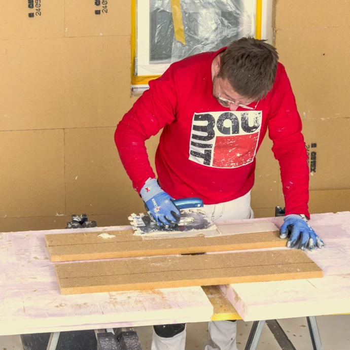 Heimwerker nutzt Baumit-Produkte, um Holzbretter auf Werkbank zu bearbeiten. Im Hintergrund Dämmmaterial an Wänden.