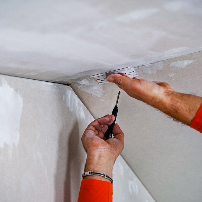 Die Trockenbaufläche wird mit einem Stück Bewegungsfugenprofil und einem Bleistift markiert.