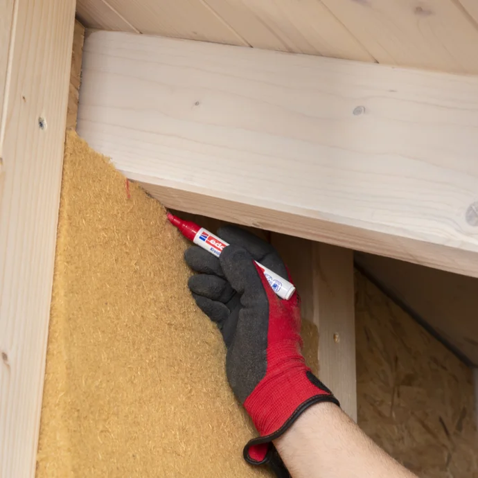 Handwerker schneidet Dämmstoff an Holzdecke passgenau zu.
