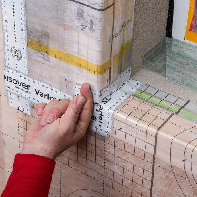 Das Klebeband von ISOVER wird zum Schluss am Fenster an der Ecke festgedrückt. So ist die Dampfbremse abgedichtet auch im Fensterbereich. Baumit Anleitung zum Thema "Dampfbremse auf eine Innendämmung mit Tragkonstruktion fachgerecht einbauen".