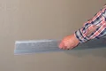 Hand richtet Metallprofil an Wand für präzise Putzanwendung aus. Ideal für gleichmäßige Oberflächen in Heimwerkerprojekten.