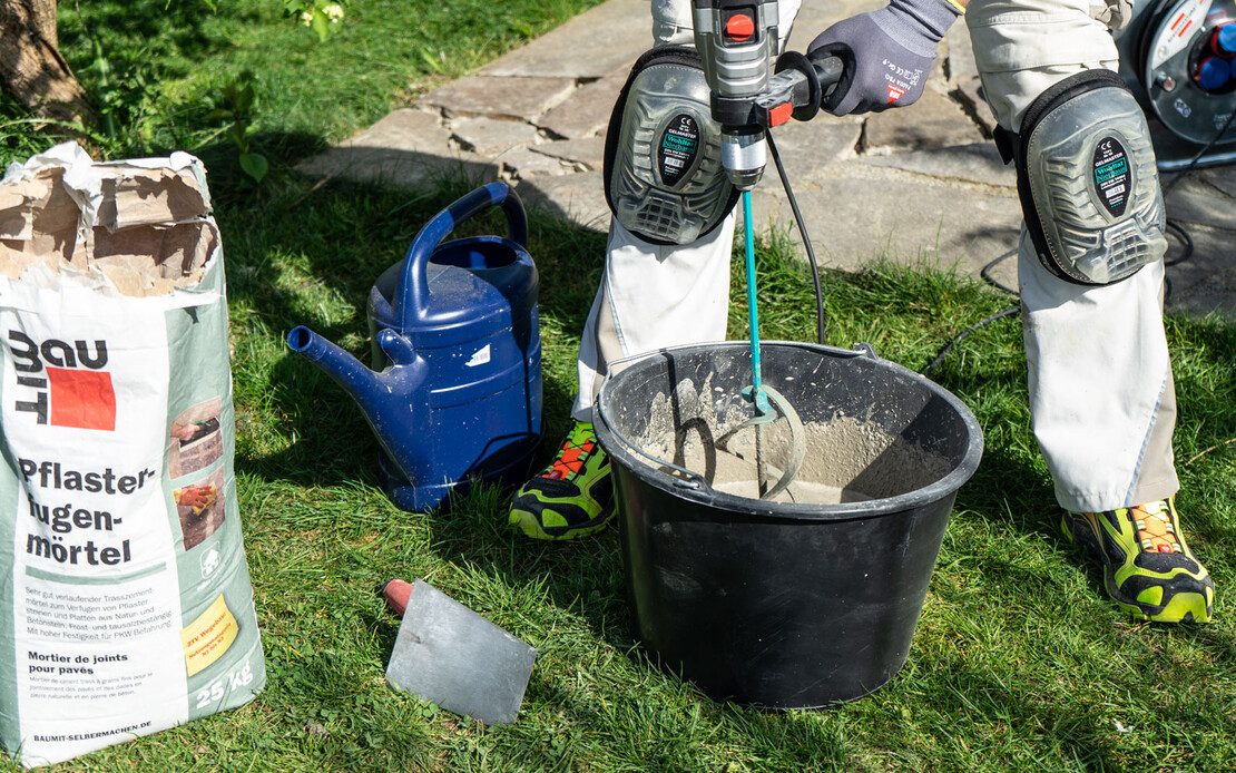 Person rührt mit einem elektrischen Rührgerät den Pflasterfugenmörtel im Garten an.