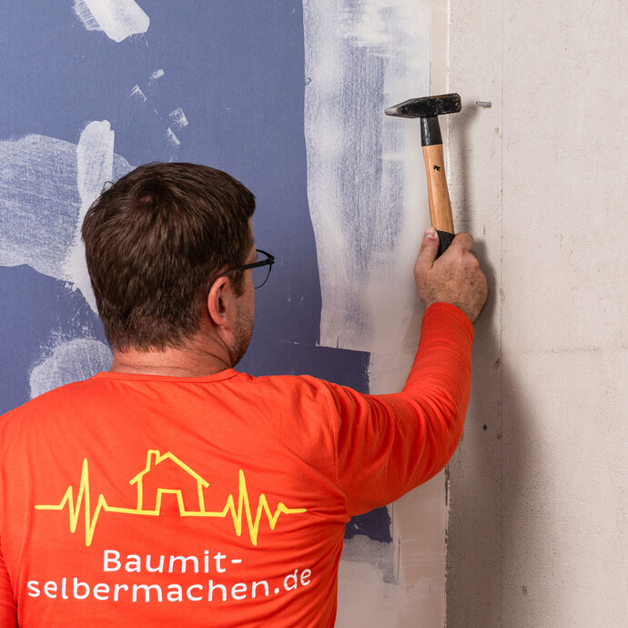 Heimwerker setzt den Dübel in das vorgebohrte Loch in die Wand und schlägt den Dübel mit dem Hammer oberflächenbündig ein.